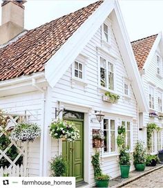 a row of white houses with green doors, windows and plants on the side of them