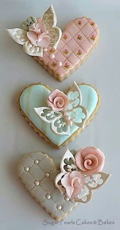 three decorated cookies in the shape of hearts and flowers on a white table with one cookie shaped like a heart