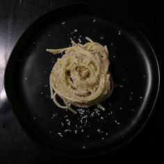 a black plate topped with pasta and parmesan sprinkled on top of it