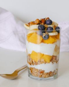 a glass filled with yogurt and fruit on top of a white table next to a spoon