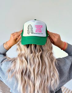 a woman with long blonde hair wearing a green and white trucker hat