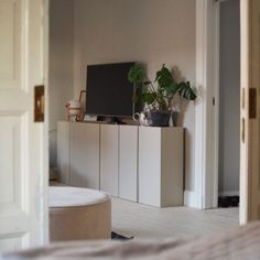 a living room with a tv, plant and white cabinets