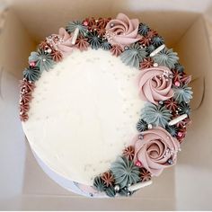 a white cake with pink and blue frosting roses on top in a cardboard box