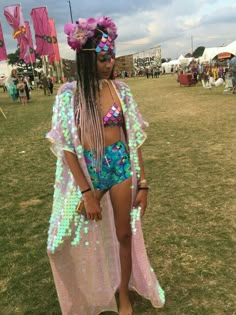 a woman in a bathing suit and headpiece standing on the grass at an outdoor music festival