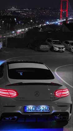 the back end of a mercedes car with its lights on at night in front of a cityscape