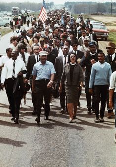 a large group of people are walking down the street with an american flag in the background