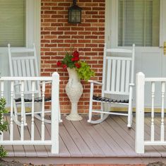 two white rocking chairs sitting on a porch next to a flower pot with flowers in it