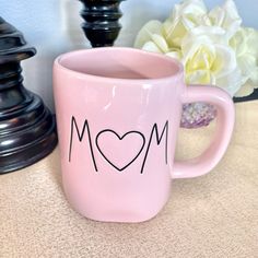 a pink coffee mug with the word mom written on it next to a white flower