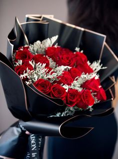 a woman holding a bouquet of red roses in her left hand and wrapped in black paper