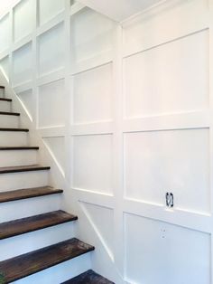 a set of wooden stairs leading up to a white painted wall with paneling on it