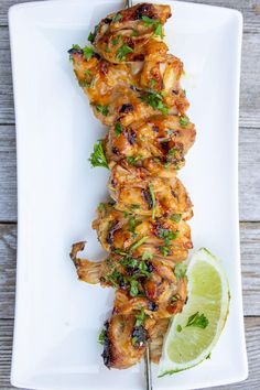 chicken skewers on a white plate with a lime wedge next to it and a slice of lime