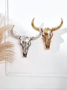 two gold and silver bull heads on a white wall next to pamodia plants