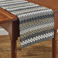 a wooden table topped with a gray and white knitted placemat on top of a wooden table