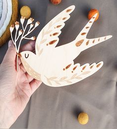 a hand holding a wooden cutout of a bird with leaves on it's wings