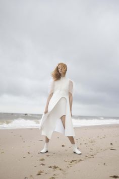 a woman standing on top of a sandy beach next to the ocean wearing a white dress