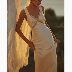 a woman in a wedding dress standing next to a wall with her hand on her hip