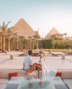 a man and woman sitting on top of a couch next to each other in front of pyramids