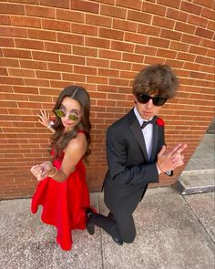 a young boy and girl dressed up in formal wear standing next to a brick wall