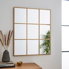 a vase with some plants in it next to a mirror on the wall above a table