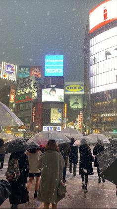 people walking in the rain with umbrellas on a busy city street at night time