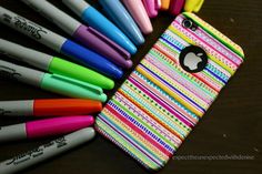 an iphone case with many pens and markers on it, sitting next to a pile of pens