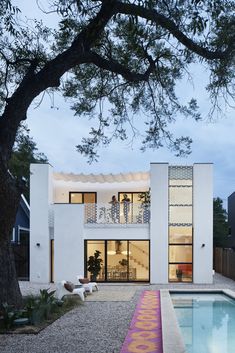 a white house with a pool in the front yard and trees around it at dusk