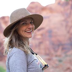 a woman wearing a hat standing in front of a rock formation and smiling at the camera