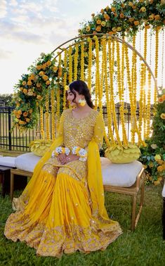 a woman sitting on top of a bench in front of a flower covered arch with yellow flowers