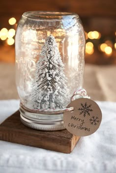 a christmas tree in a glass jar on top of a wooden block with a tag