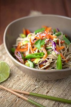 a bowl filled with noodles and vegetables on top of a table next to a lime slice