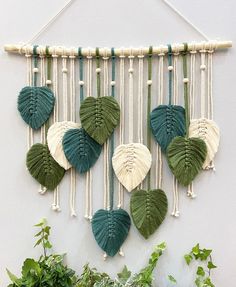 a green and white wall hanging with leaves on it next to some potted plants