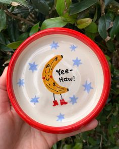 a hand holding a small bowl with a banana painted on the side and words yee - haw written on it