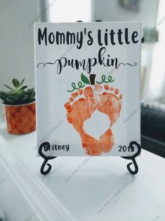 a sign that says mommy's little pumpkin feet on top of a table next to a potted plant