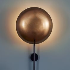 a round light fixture mounted to the side of a white wall with a metal pole