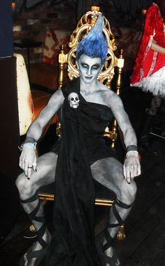 a man with blue hair sitting in a chair wearing skeleton makeup and headdress