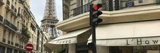 the traffic light is red in front of the eiffel tower and people are walking down the street