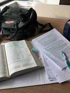 an open book sitting on top of a table next to a bag and some papers