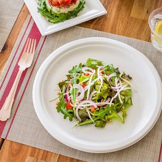 a white plate topped with salad on top of a wooden table next to a glass of water