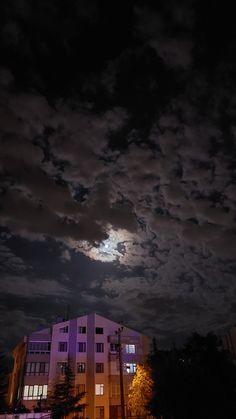 the moon is shining brightly in the night sky over a building with windows and trees