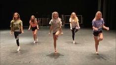 five young women are dancing on stage in short skirts and t - shirts, with one woman holding her leg up