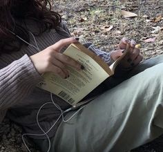 a woman sitting on the ground reading a book with headphones attached to her ears