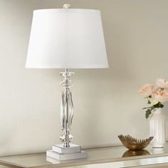 a white lamp sitting on top of a glass table next to a vase with flowers