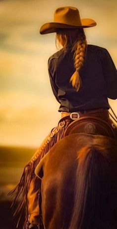 a woman wearing a cowboy hat sitting on top of a brown horse