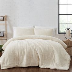 a bed with white linens and pillows in a room next to a brick wall