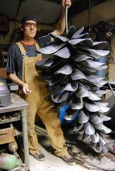 a man in overalls holding up a large pile of metal parts on a workbench