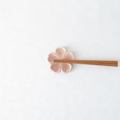 two chopsticks and a flower shaped brooch on a white surface