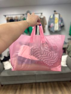 a person holding a pink shopping bag in their hand with clothes on the wall behind it