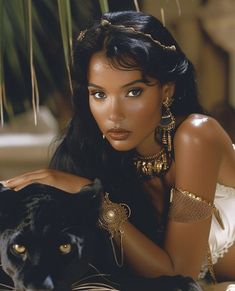 a beautiful woman laying on top of a bed next to a black cat wearing gold jewelry