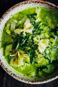 a white bowl filled with pasta and spinach in pesto sauce on top of a wooden table