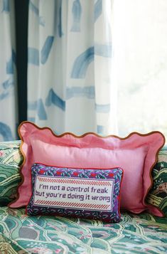 a pink pillow sitting on top of a bed next to a blue and white curtain